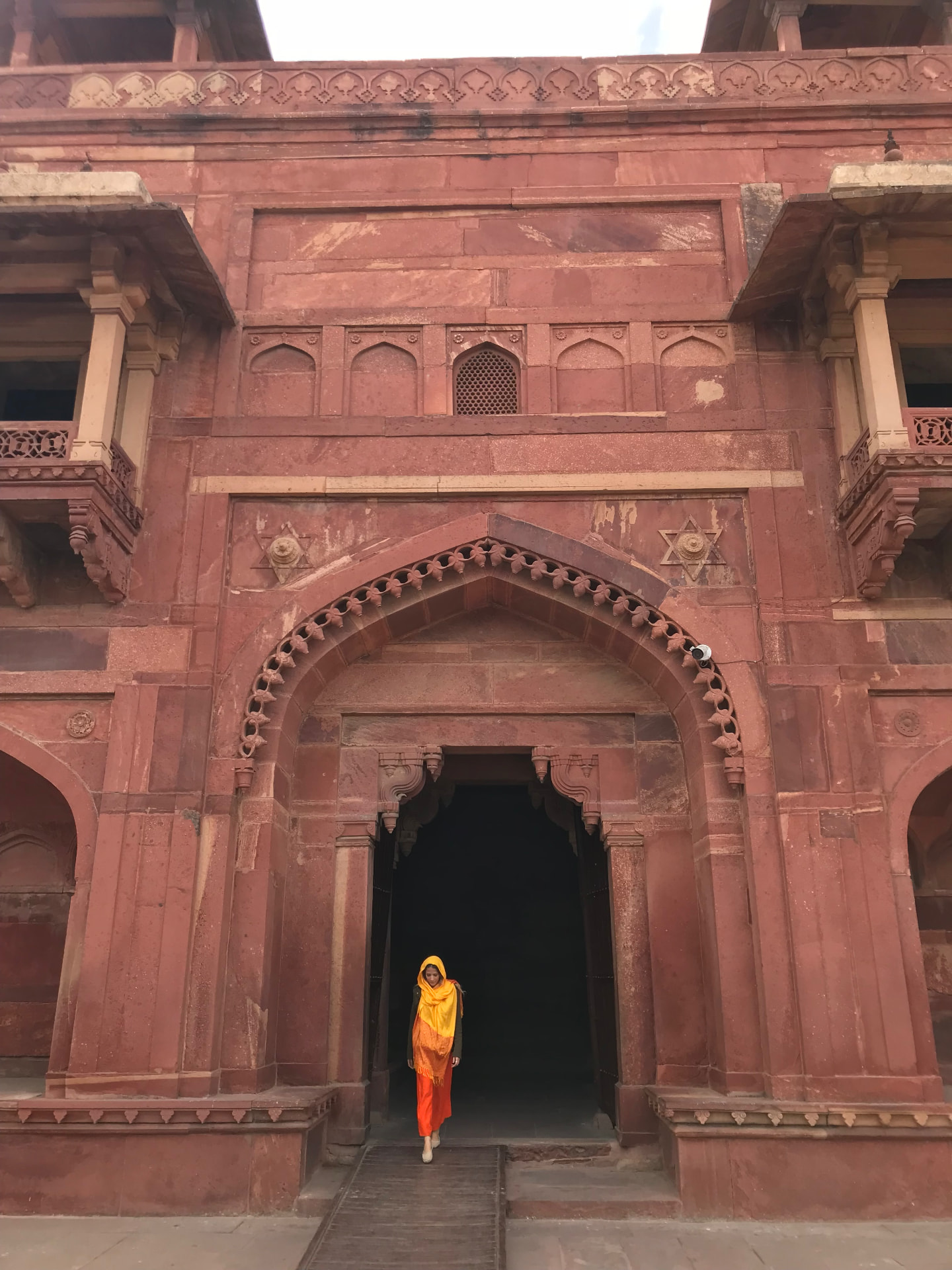 Nina de véu laranja saindo do arco de arenito vermelho de Fatehpur Sikri
